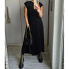A woman wearing a black sleeveless pleated midi dress and black boots standing in a hallway.