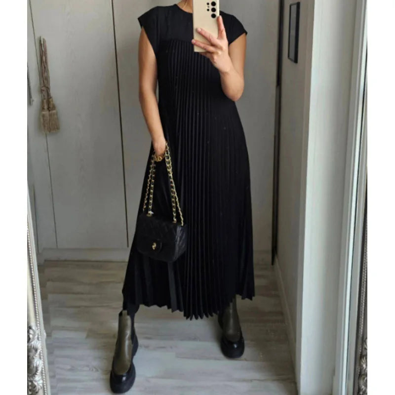 A woman wearing a black sleeveless pleated midi dress and black boots standing in a hallway.