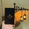 A black decorative sign featuring a gold fleur-de-lis emblem is held against a warm glowing vintage library lantern shelf lam