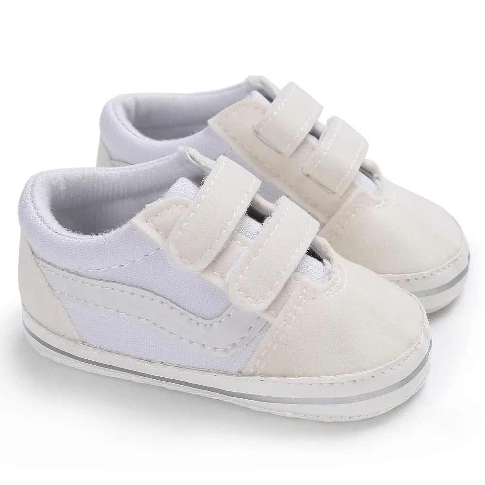 A pair of light gray canvas baby sneakers with white laces and a white sole.