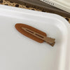 A pair of matte resin side hair clips in a tan or brown color resting on a white tray.