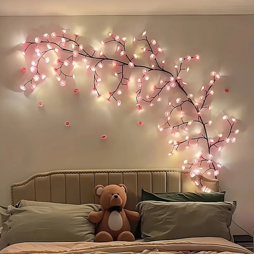 Vägglampa i grenform med rosa körsbärsblomsljus ovanför en säng.