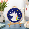Kit de bordado de punch needle arcoíris con diseño de unicornio blanco sobre fondo azul oscuro.