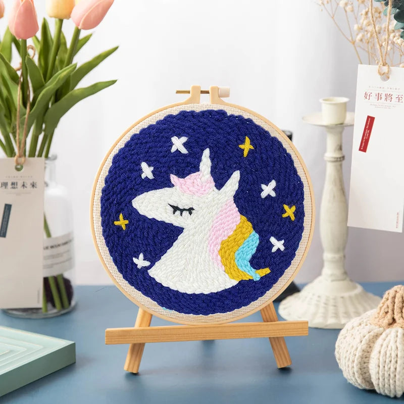 Kit de bordado de punch needle arcoíris con diseño de unicornio blanco sobre fondo azul oscuro.