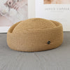A beige straw pillbox sun hat with a wide brim resting on a gray surface.