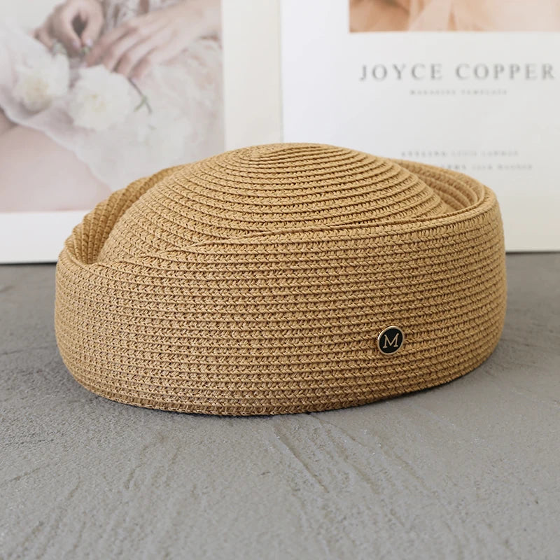 A beige straw pillbox sun hat with a wide brim resting on a gray surface.