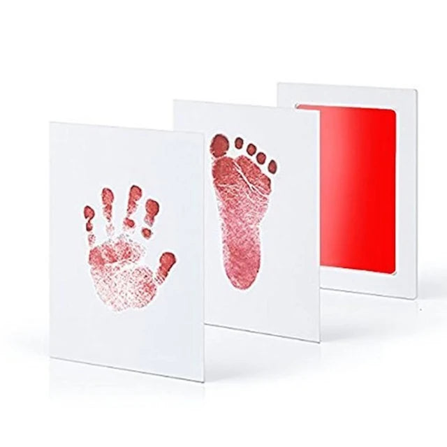 A set of white framed prints showing a pink handprint and a pink footprint impression on the paper.