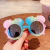 A hand holds a pair of colorful kids polarized sunglasses with pink and blue frames.