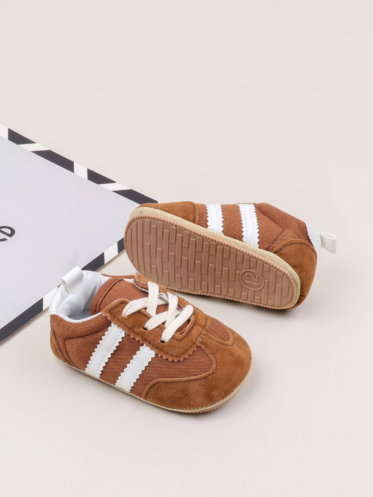 A pair of brown baby first walker shoes with white stripes and an anti-slip TPR sole resting on a white background.