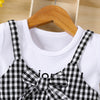 White cotton knit dress with black plaid accent and bow displayed on a wooden hanger.