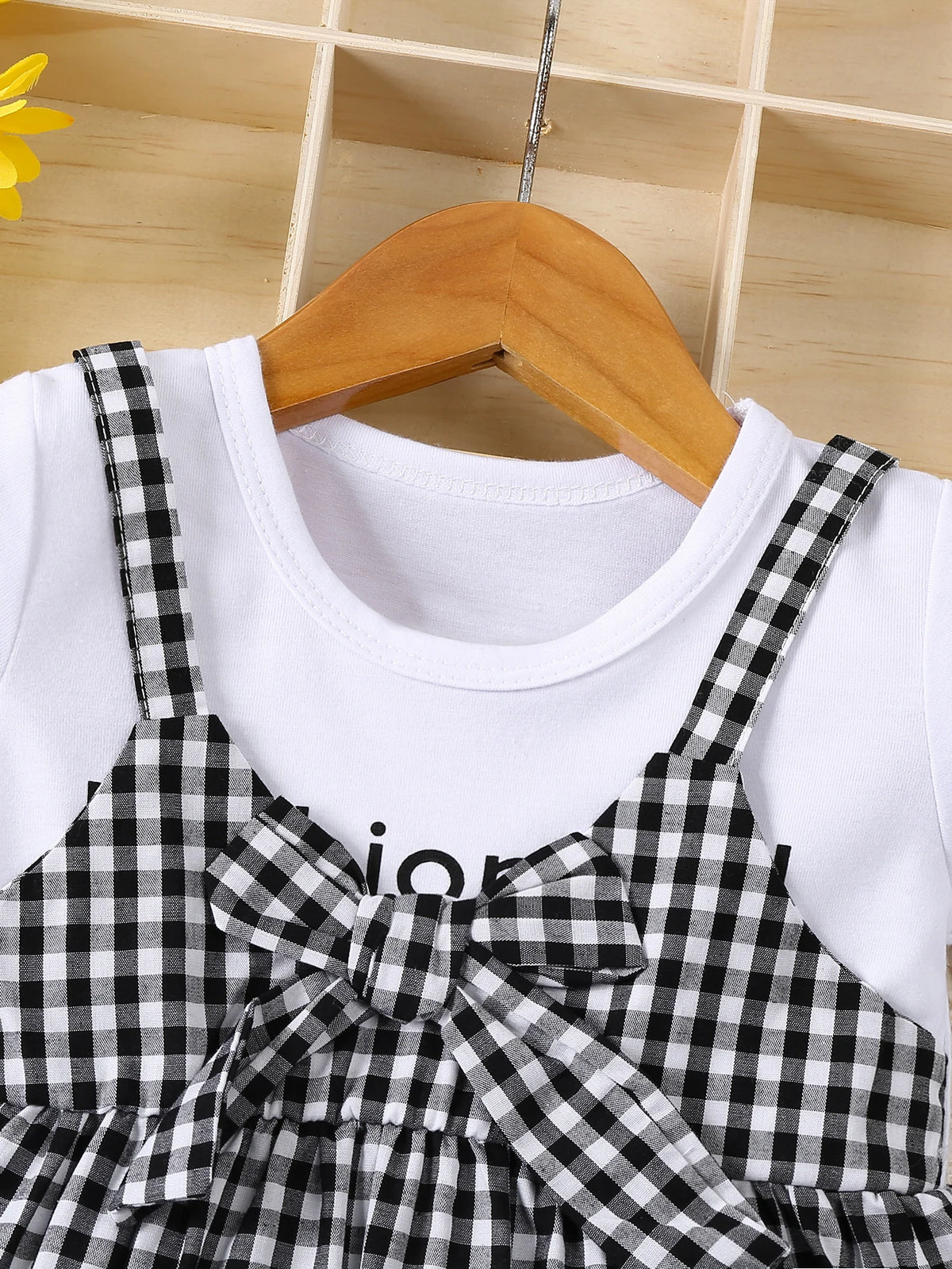 White cotton knit dress with black plaid accent and bow displayed on a wooden hanger.