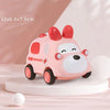 A pink soft rubber toy car with large ears and wheels is displayed on a white surface.