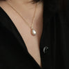 A close-up of a sterling silver water droplet pendant necklace with a zircon stone worn on a person's chest.