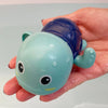 A hand holds a blue and light green bath toy shaped like a duck or penguin with water spray features.