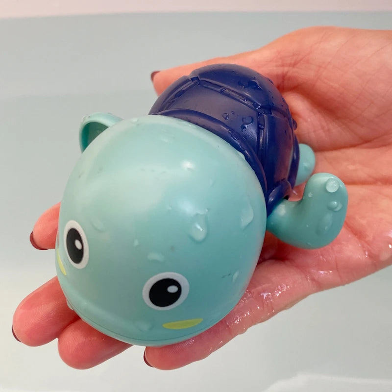 A hand holds a blue and light green bath toy shaped like a duck or penguin with water spray features.