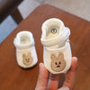 A pair of white soft-sole sandals for a baby, featuring a bear design on the toe.