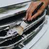 A hand is using a detailing brush to clean the exterior of a car's grille.