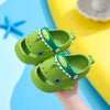 A pair of green shark clog sandals for kids with a happy face design