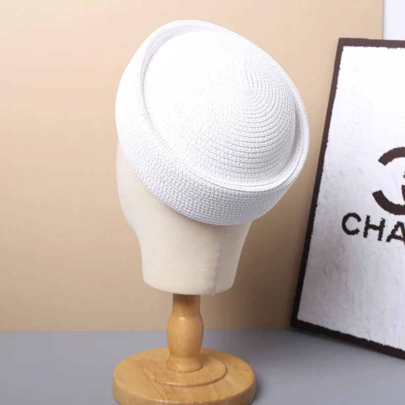 A white straw pillbox sun hat displayed on a mannequin against a light background.