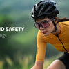 A woman wearing a yellow long-sleeved athletic top and sunglasses is cycling outdoors, emphasizing comfort and safety.