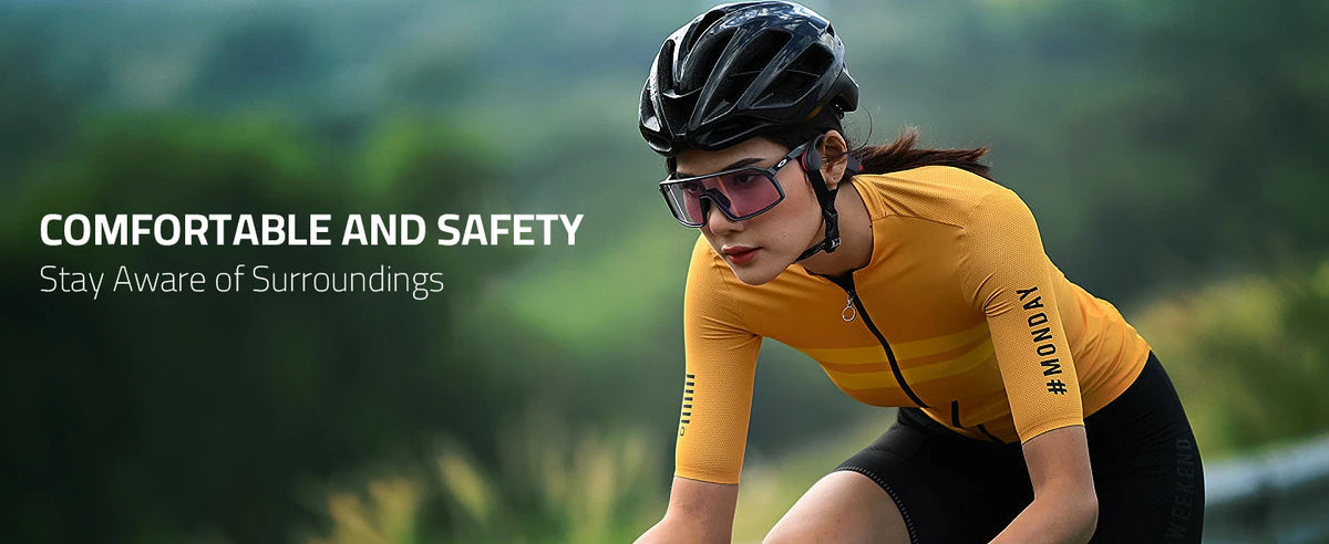 A woman wearing a yellow long-sleeved athletic top and sunglasses is cycling outdoors, emphasizing comfort and safety.