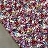 Close-up of floral 100% cotton poplin fabric featuring a dense pattern of pink, red, yellow, and blue flowers.