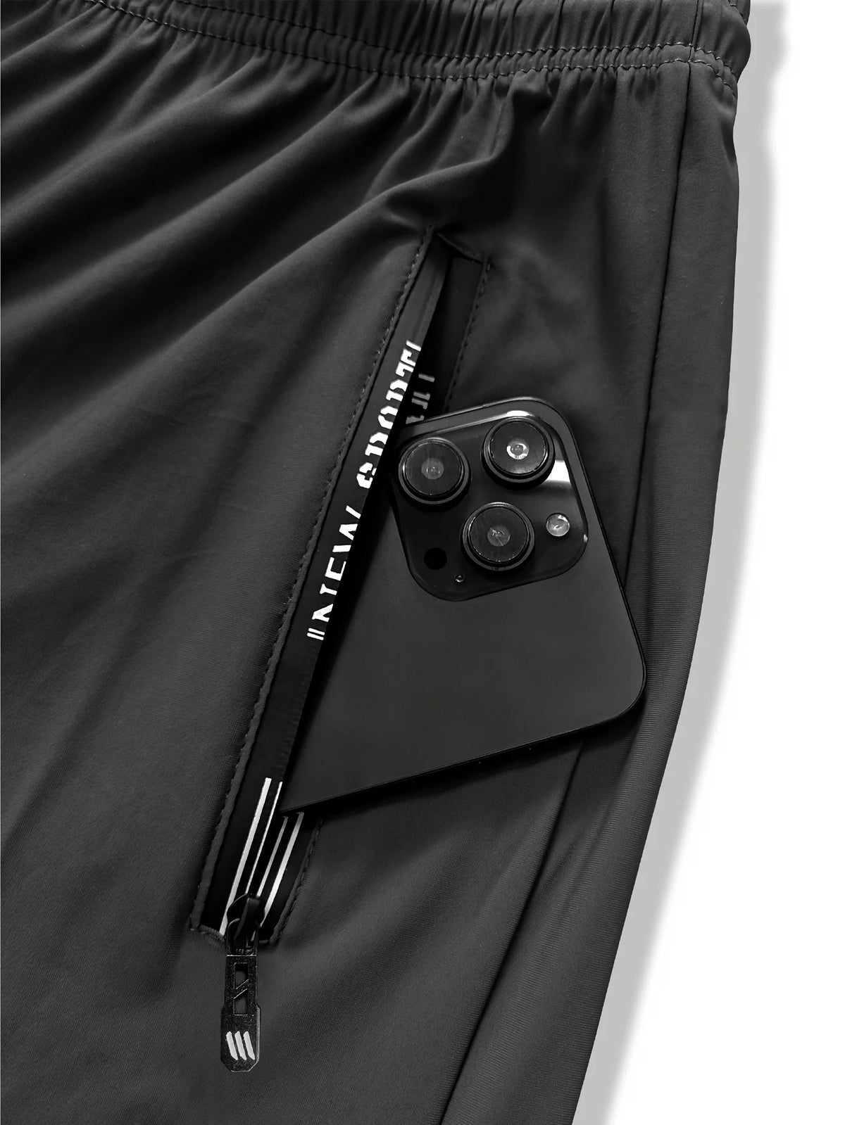 A close-up of black men's high-stretch joggers showing a zippered pocket with an attached smartphone.