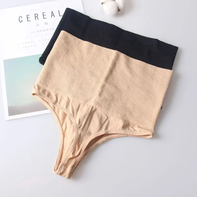 A beige high-waist thong shaper and black underwear are displayed on a white surface.