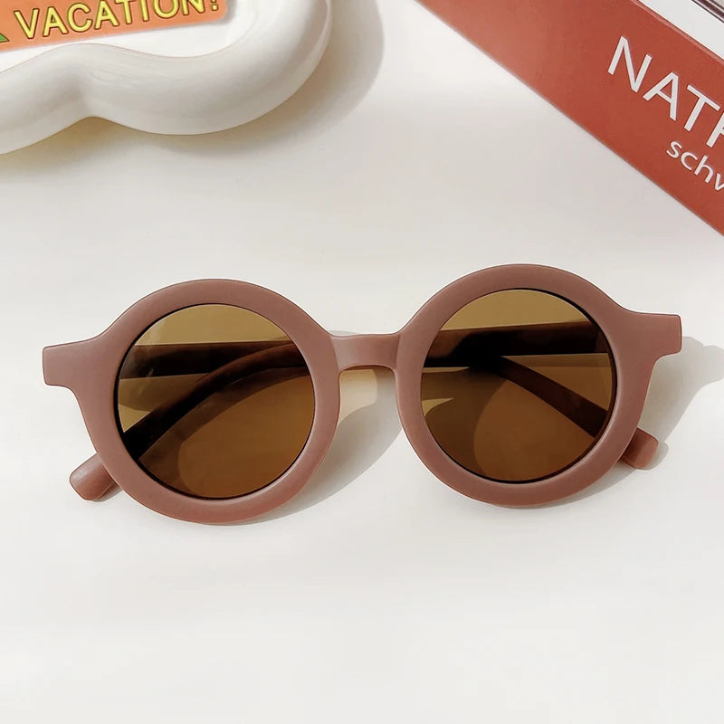 A pair of rose gold-toned sunglasses with brown lenses resting on a white surface.