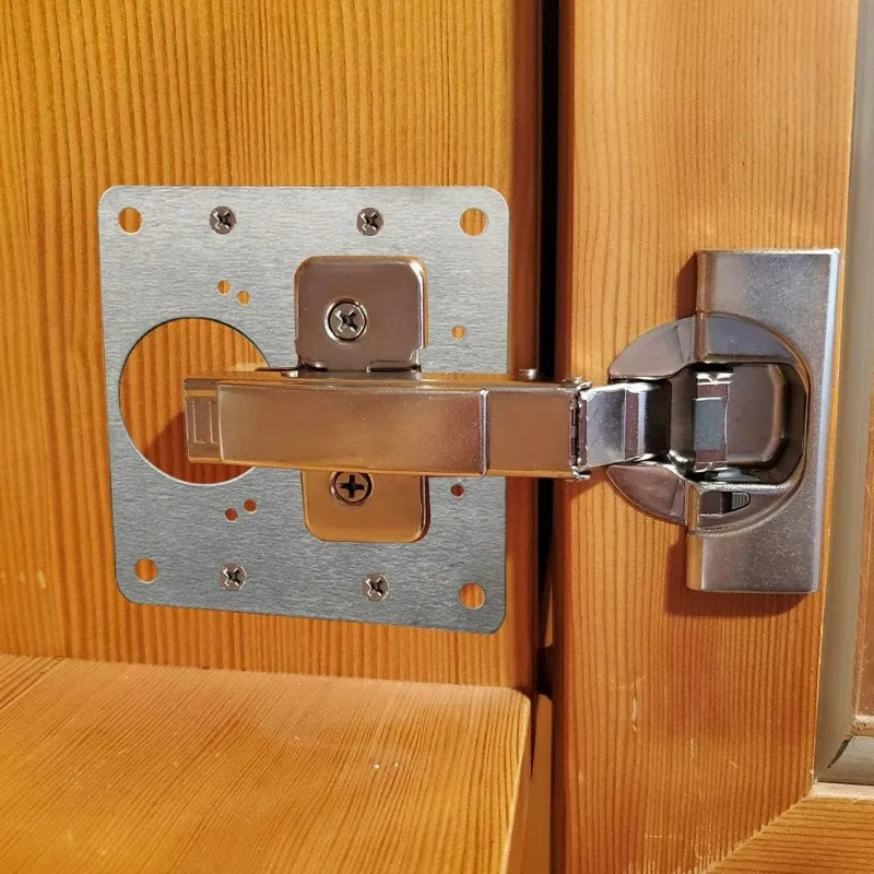 Stainless steel cabinet door hinge repair plate kit with screws attached to a wooden door frame.