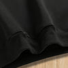 A close-up of a black pullover hoodie with a ribbed cuff and a letter print detail.