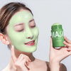 A woman applies a green tea cleansing stick mask to her face, holding the product container.