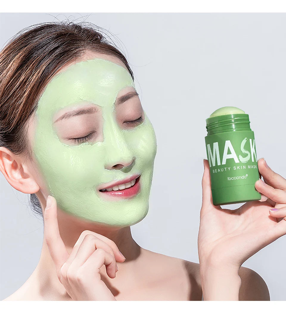 A woman applies a green tea cleansing stick mask to her face, holding the product container.