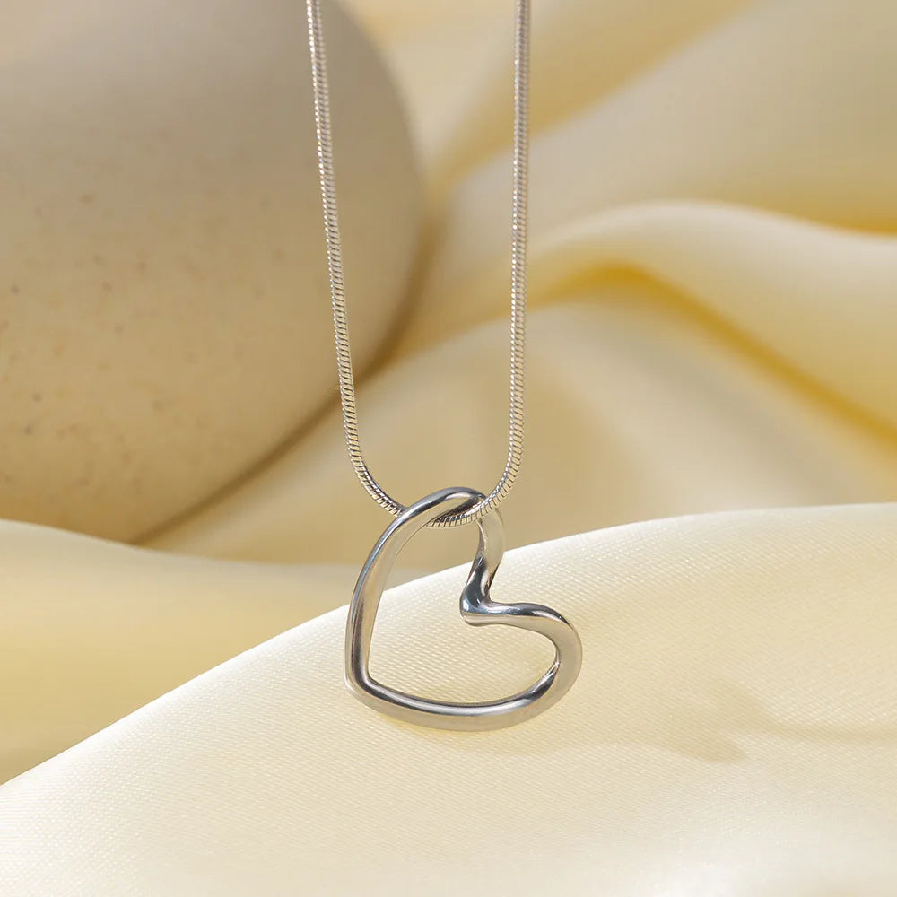 A dainty gold heart pendant necklace with a snake chain resting on soft yellow fabric.