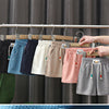 A hand is hanging various colored kids beach shorts on a clothes rack.