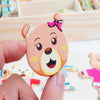 A hand holds a pink wooden puzzle shaped like a bear with a pink bow for a Montessori dress-up toy.