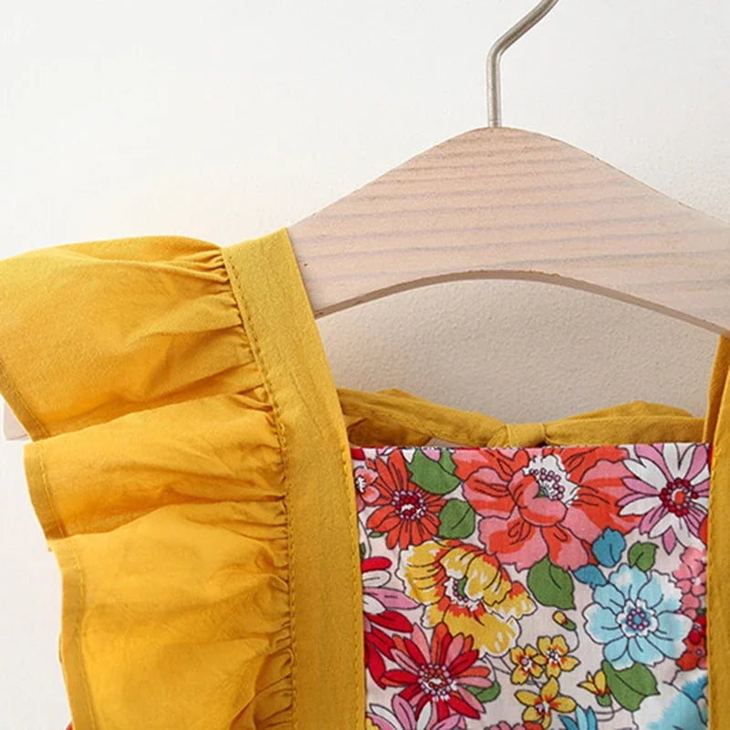 A yellow baby girl's dress with a floral print and matching hat hanging on a wooden hanger.