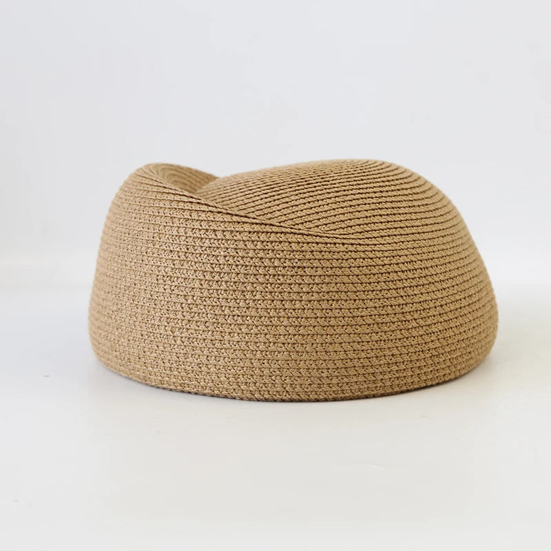 A beige straw pillbox sun hat with a wide brim, shown from the side.