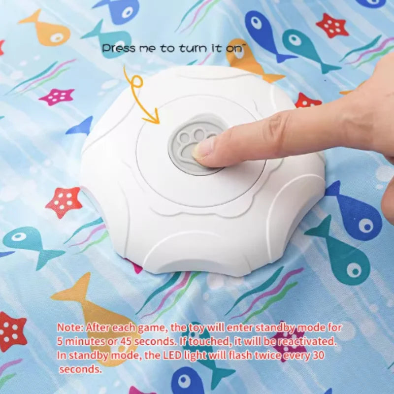 A hand presses a button on a white motion-activated cat toy, which is designed for hide and seek games.