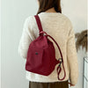A woman wearing a cream knit sweater carries a maroon mini backpack with a leather strap.