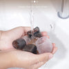 Hands hold silicone furniture leg pads with felt bottoms being rinsed under water.