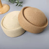 A close-up view of a beige straw pillbox sun hat with a wide brim resting on a gray surface.