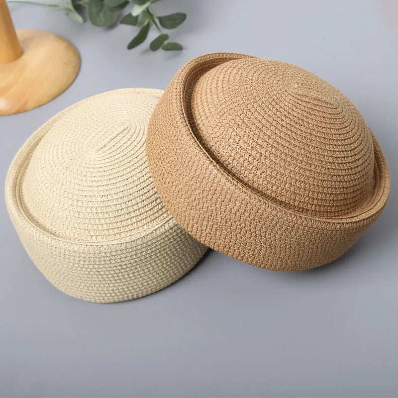 A close-up view of a beige straw pillbox sun hat with a wide brim resting on a gray surface.