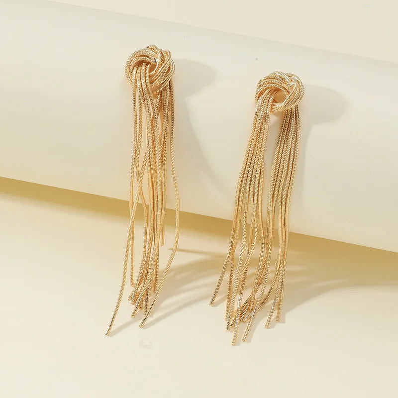 A pair of gold geometric tassel drop earrings displayed against a light background.