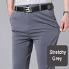 Grey stretch trousers with a black belt and a white patterned shirt being worn by a man.