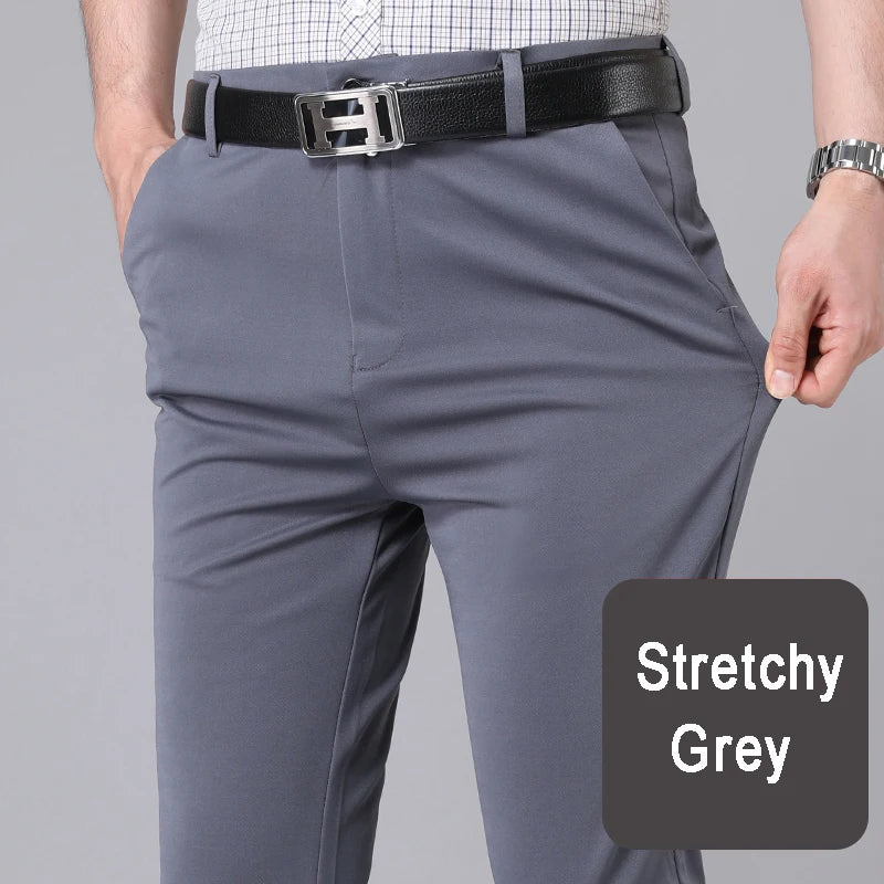 Grey stretch trousers with a black belt and a white patterned shirt being worn by a man.