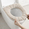 A hand is placing a beige, textured acrylic toilet seat cover onto a white toilet bowl.