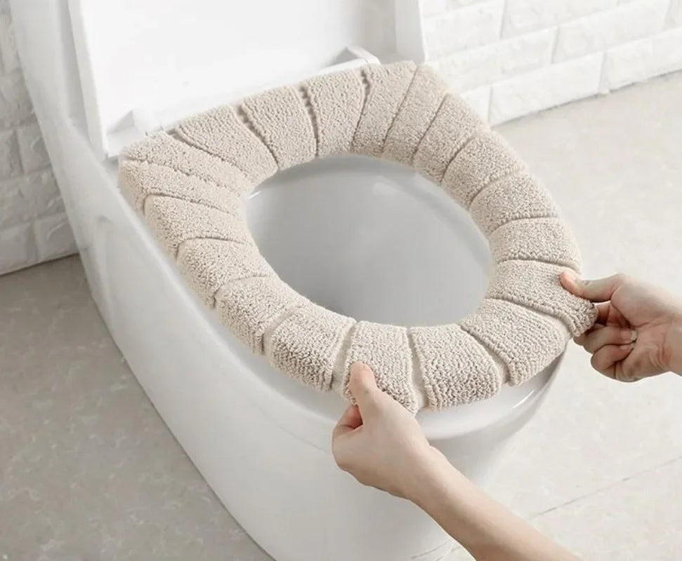 A hand is placing a beige, textured acrylic toilet seat cover onto a white toilet bowl.