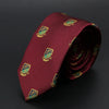 Corbata jacquard granate con emblemas bordados en oro, enrollada y sobre fondo oscuro.