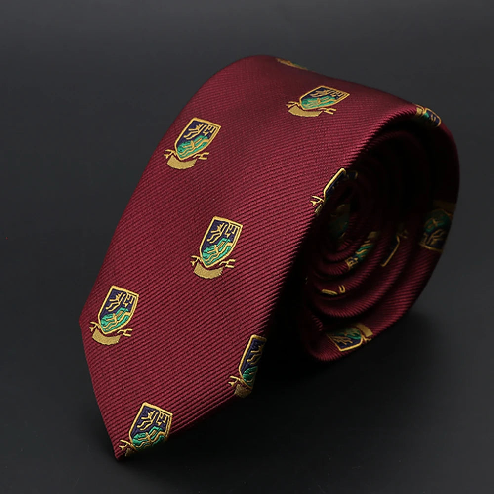 Corbata jacquard granate con emblemas bordados en oro, enrollada y sobre fondo oscuro.